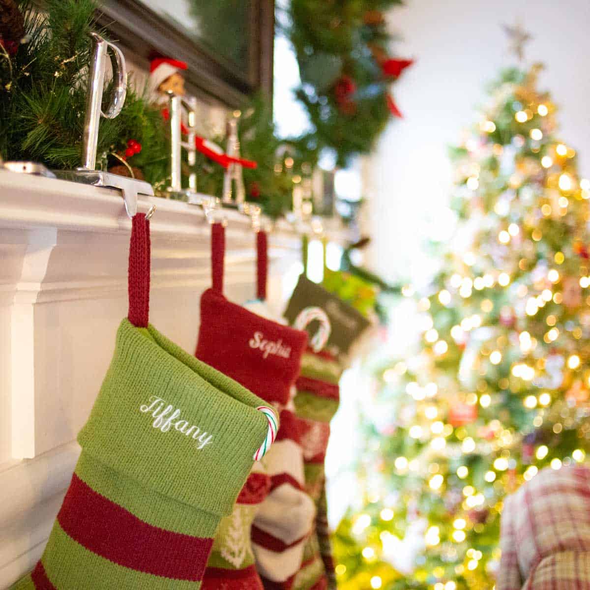 A row of stockings are hung on a mantle in front of a Christmas tree.