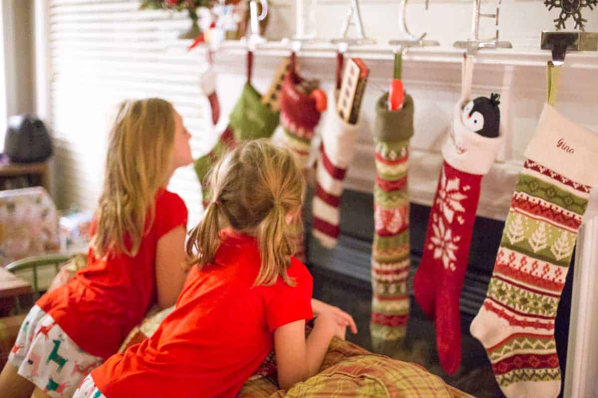 Two young girls peek at the filled stockings on the mantel.