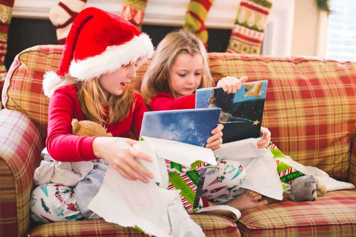 Two girls are opening a present from St. Nick, one is wearing a Santa hat.