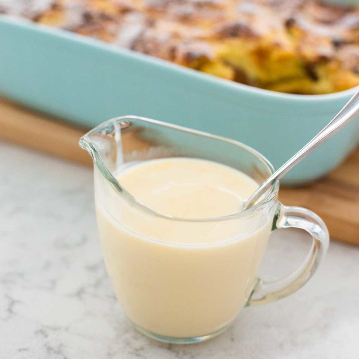 A small pitcher is filled with creamy amaretto sauce. It is on the counter in front of a panettone bread pudding.