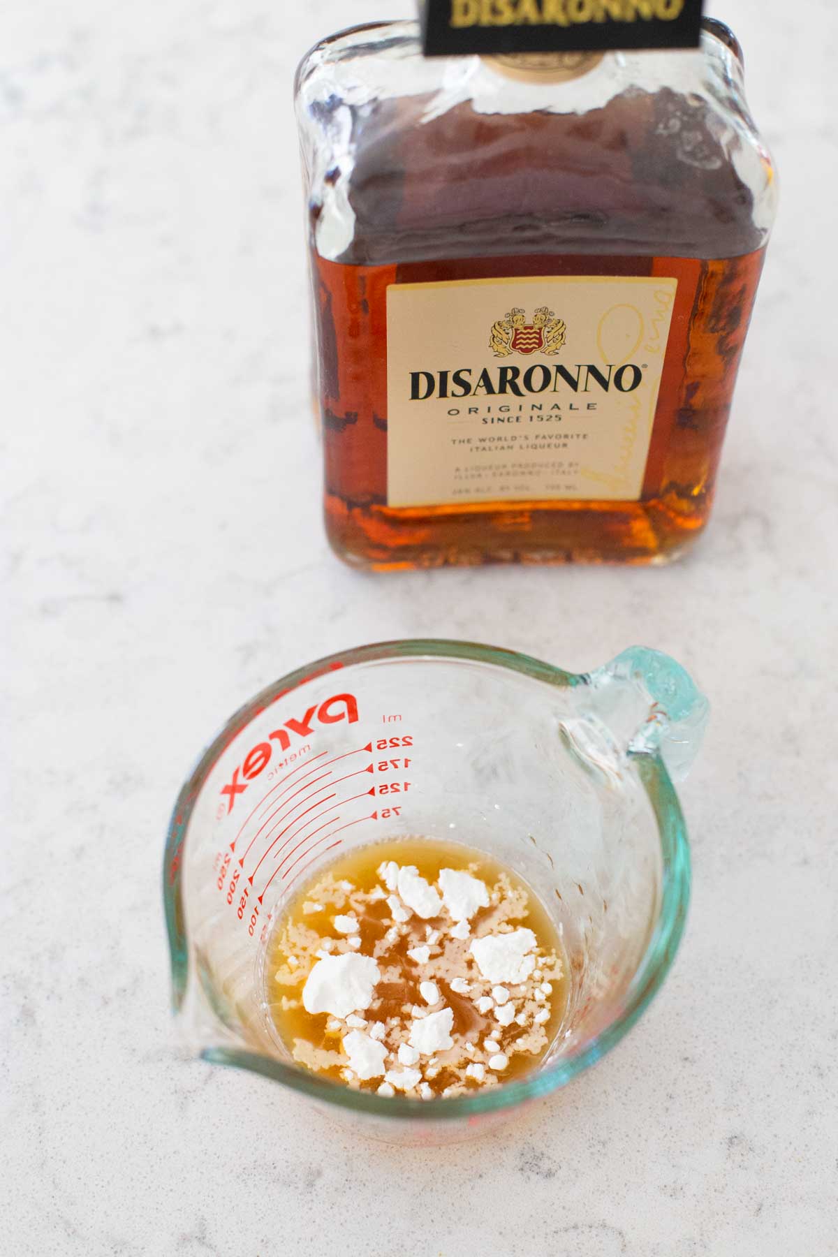 A measuring cup filled with amaretto liqueur has cornstarch sprinkled over the top.