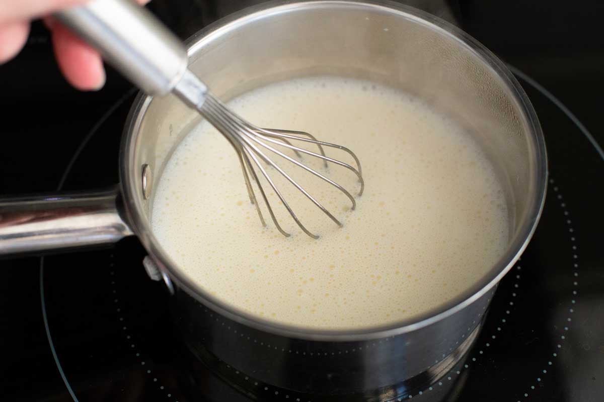 A whisk is stirring the sauce as it cooks in a saucepan on the stovetop.