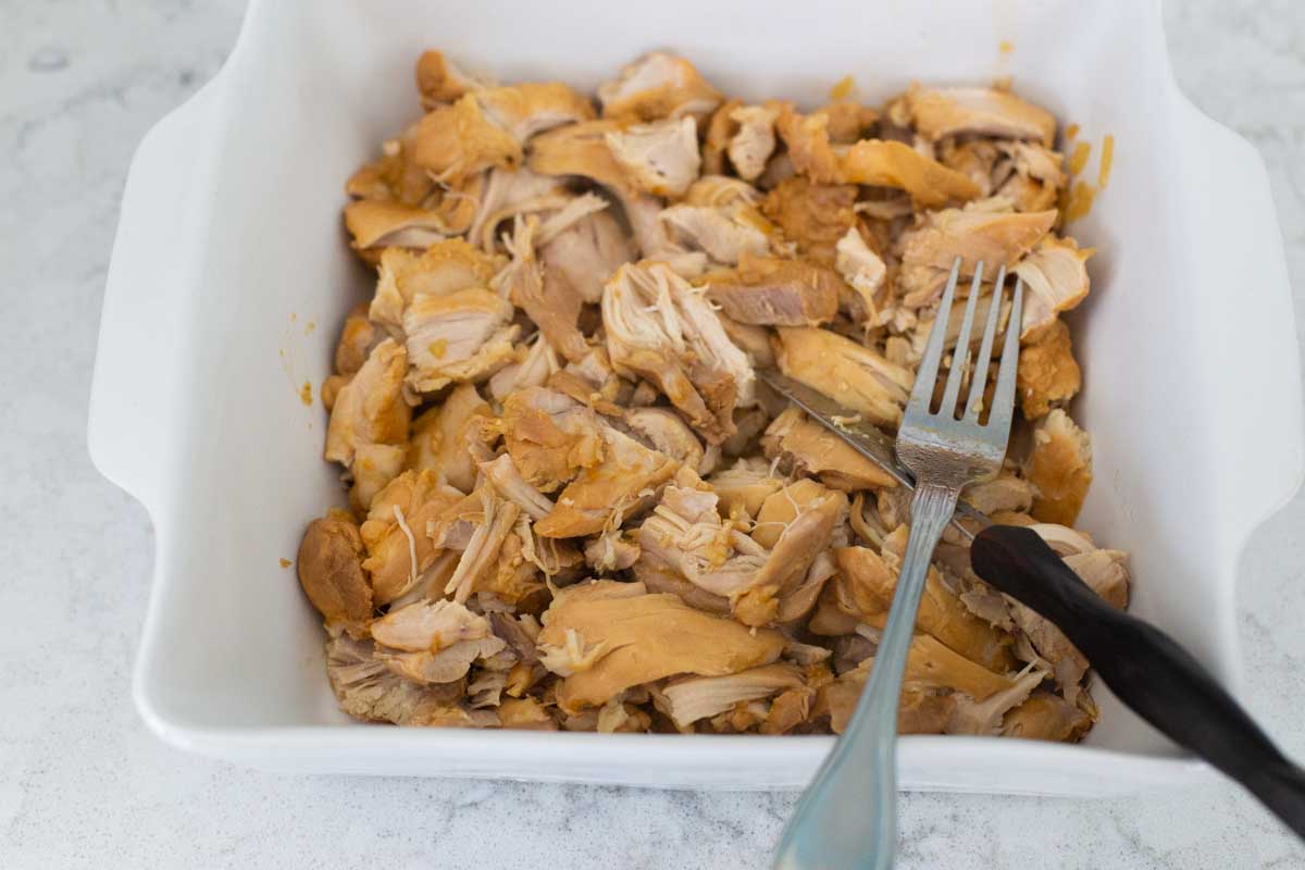 The chicken has been moved to a baking dish to be cut with a knife and fork.