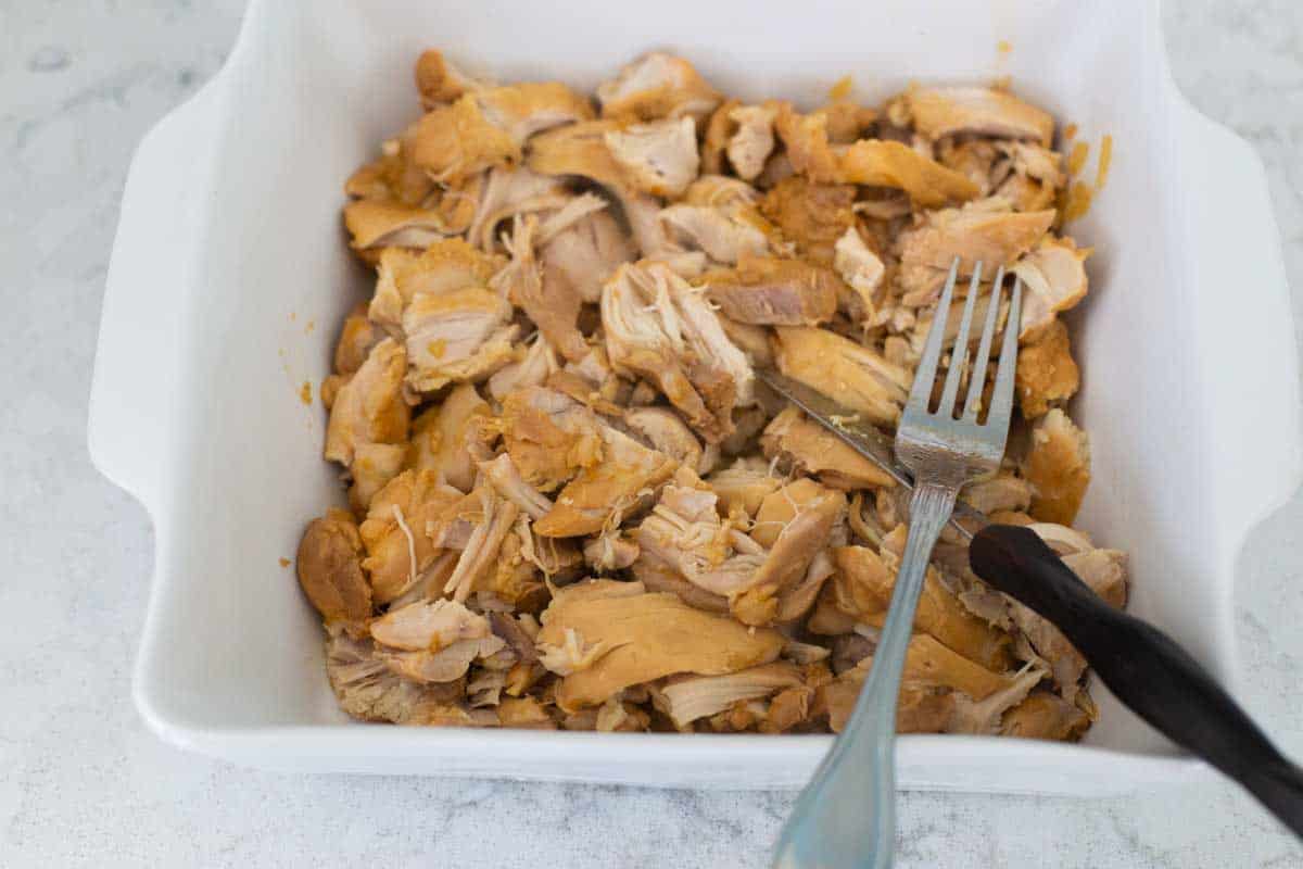 The chicken has been moved to a baking dish to be cut with a knife and fork.