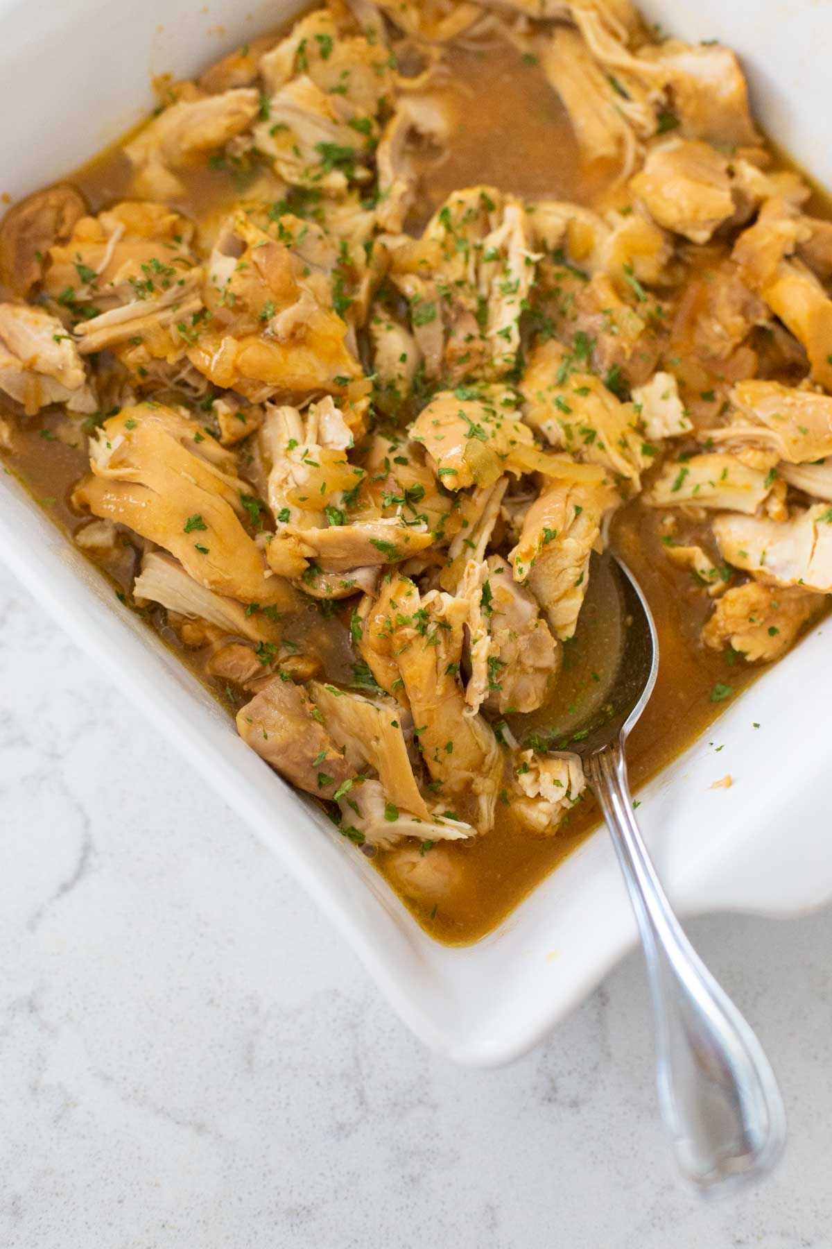 The baking dish of chicken has been coated with apricot sauce and sprinkled with fresh herbs.
