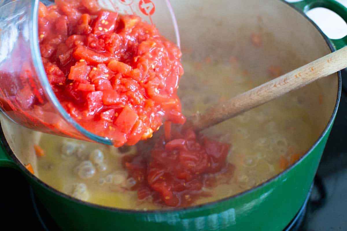 Diced tomatoes are being poured into the large dutch oven.