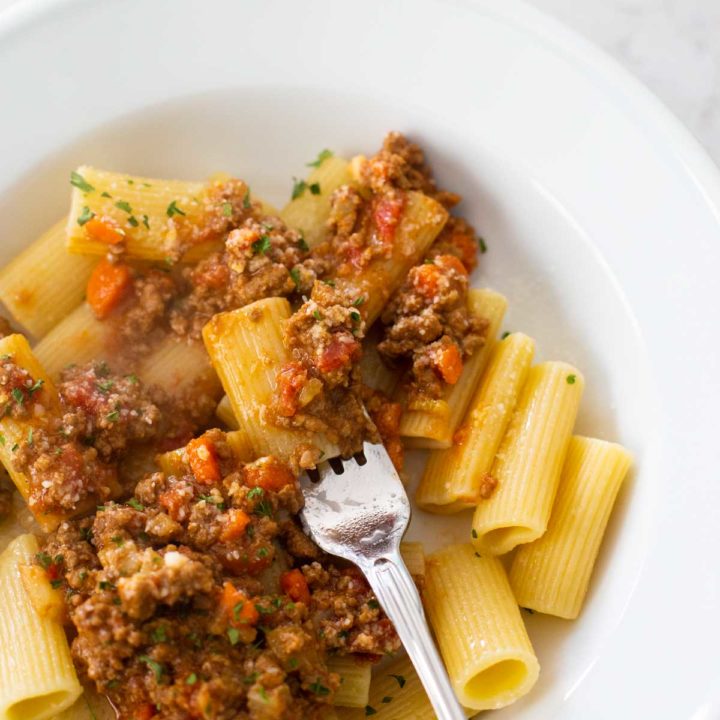 Bolognese Meat Sauce has been served over large rigatoni noodles and a fork is stirring them together.
