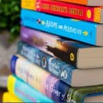 A stack of book club books next to a green plant.