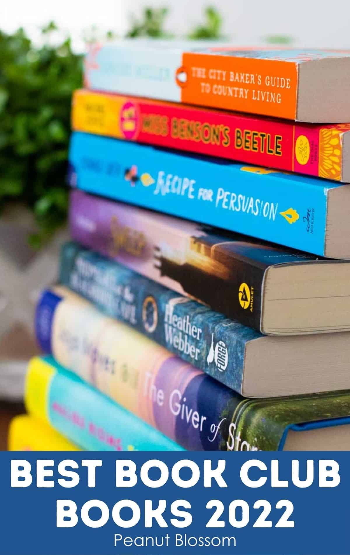 A stack of book club books next to a green plant.