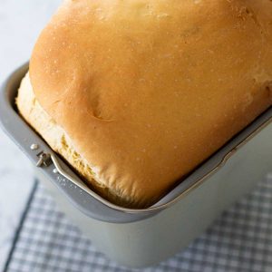 A fresh baked challah loaf is in the bread machine pan cooling on a wire rack.