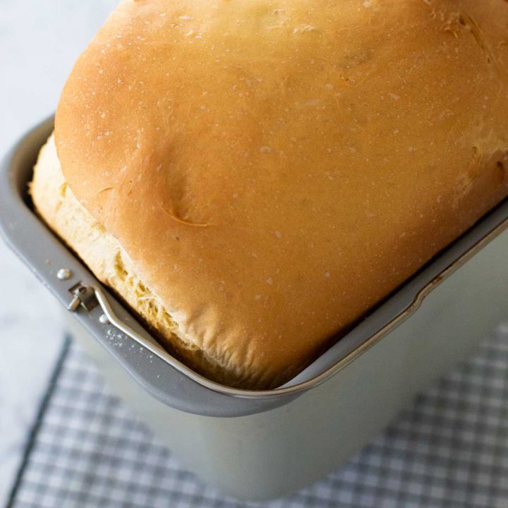 A fresh baked challah loaf is in the bread machine pan cooling on a wire rack.