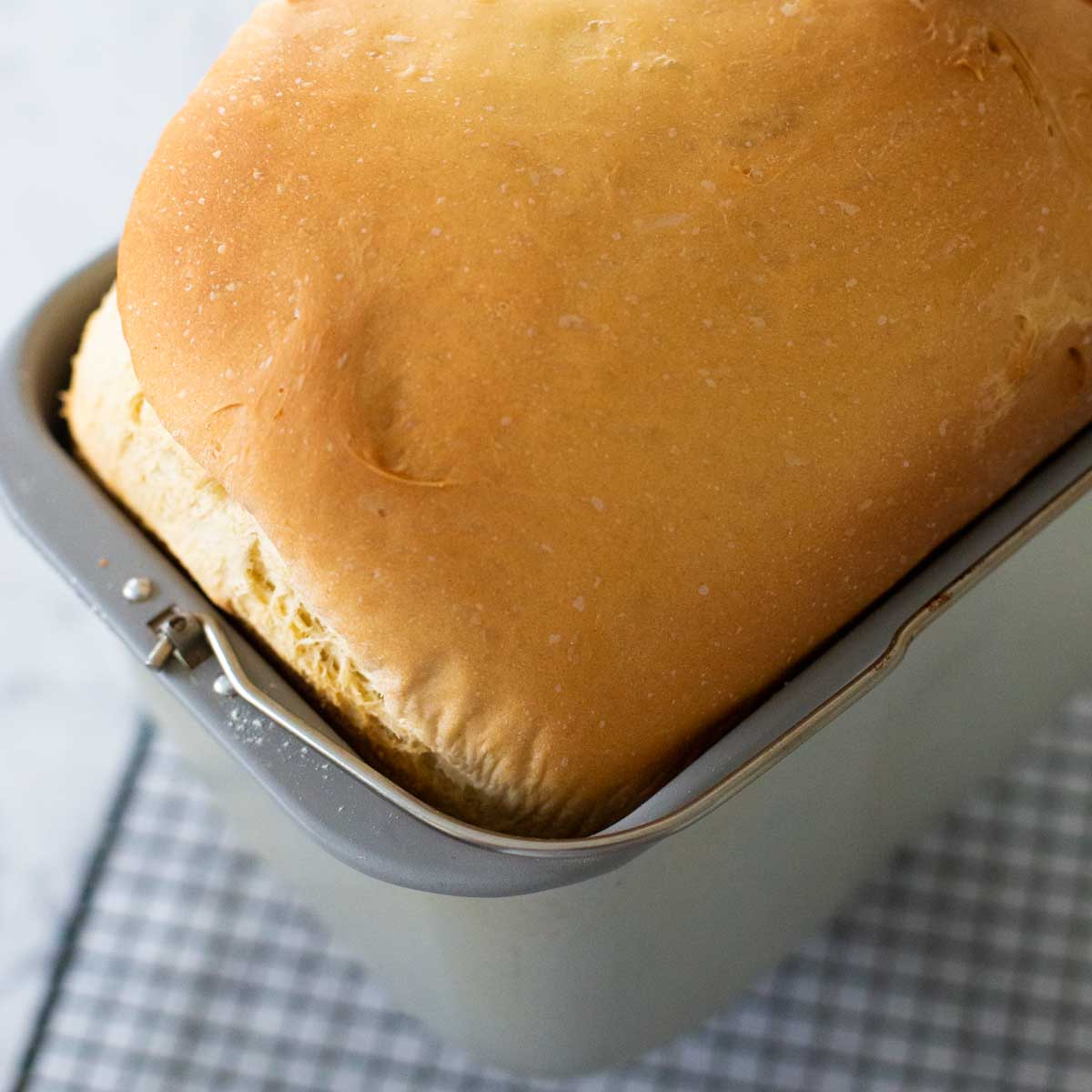 A fresh baked challah loaf is in the bread machine pan cooling on a wire rack.