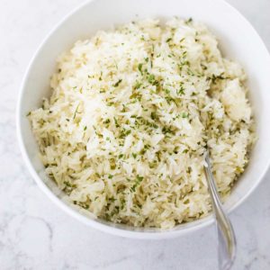 A white bowl is filled with herb butter rice and a spoon.