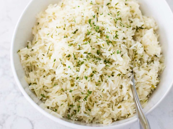A white bowl is filled with herb butter rice and a spoon.
