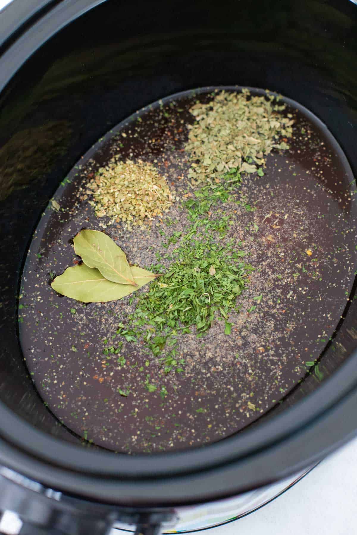 The slowcooker pot has been filled with beef broth and seasonings.