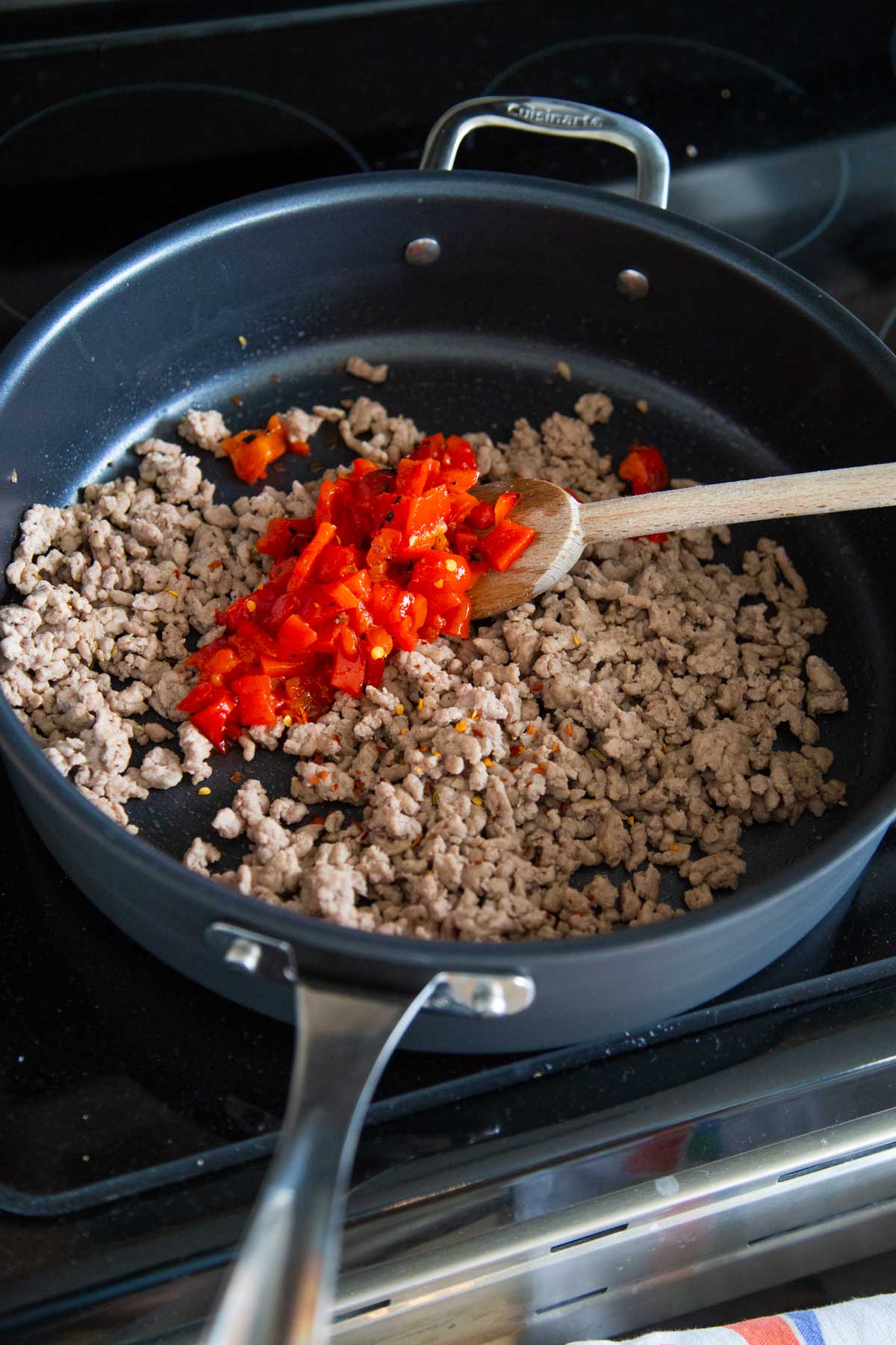 A skillet has browned, crumbled sausage and is mixing in some fresh peppers.