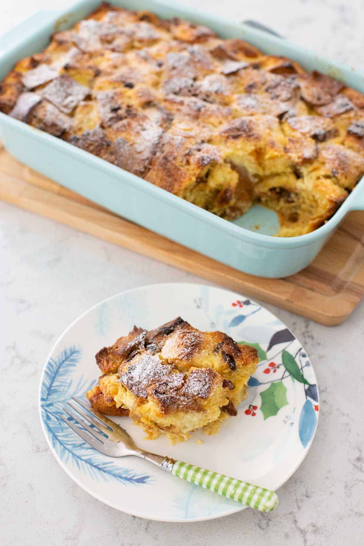 A serving of the panettone bread pudding is on a holiday plate with a fork in front of the baking dish.