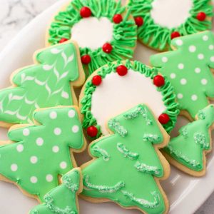 A platter of green Christmas tree sugar cookies have been decorated with royal icing in simple patterns.