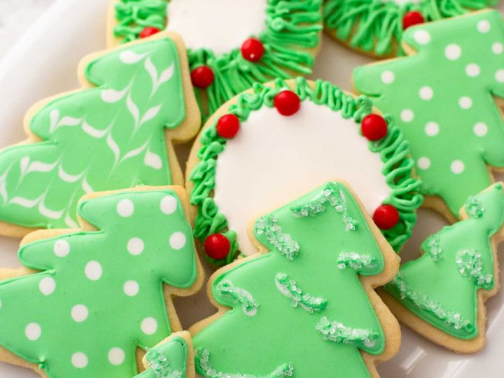 A platter of green Christmas tree sugar cookies have been decorated with royal icing in simple patterns.