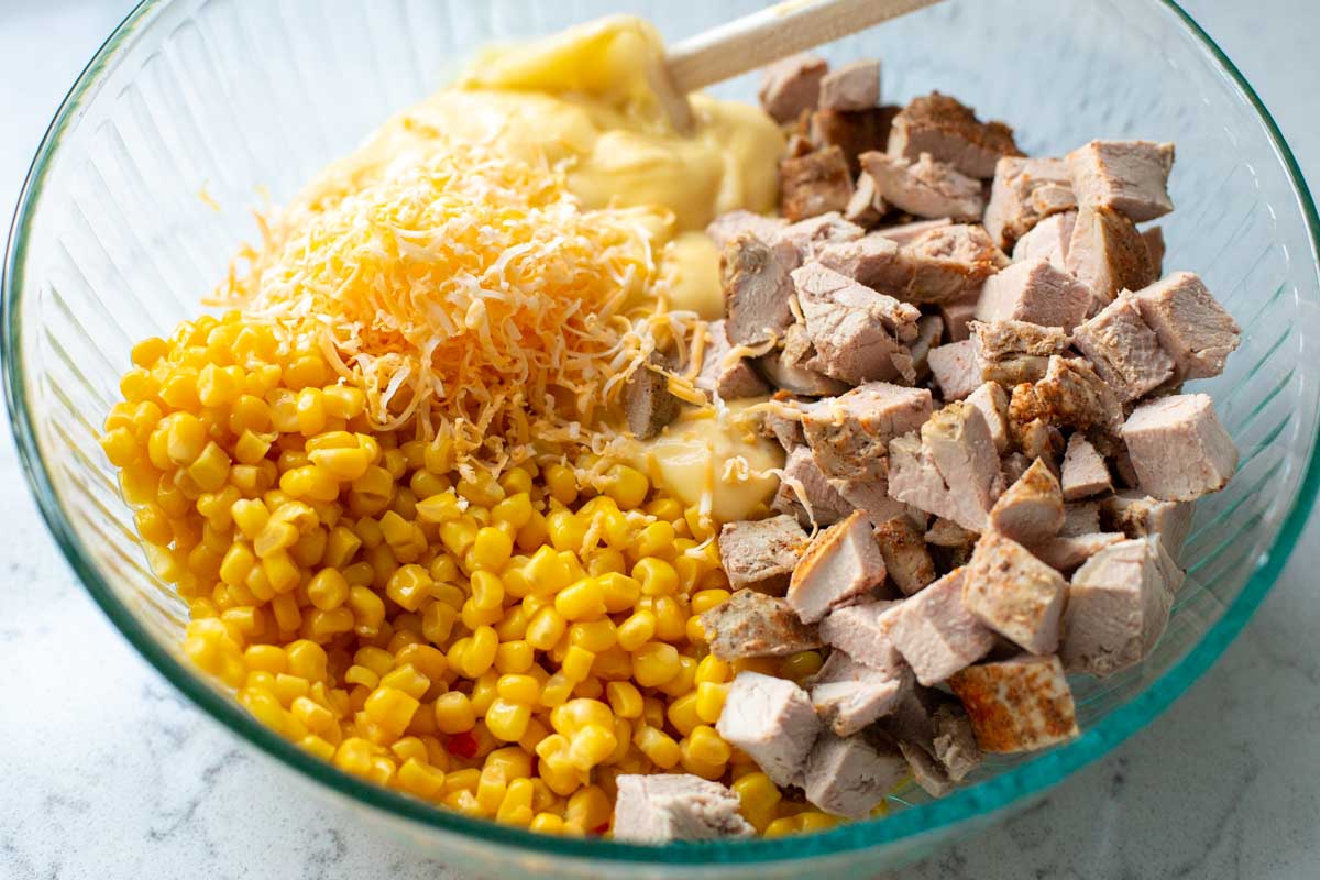 The corn, pork, condensed soup, and shredded cheese are in a very large mixing bowl with a spoon.