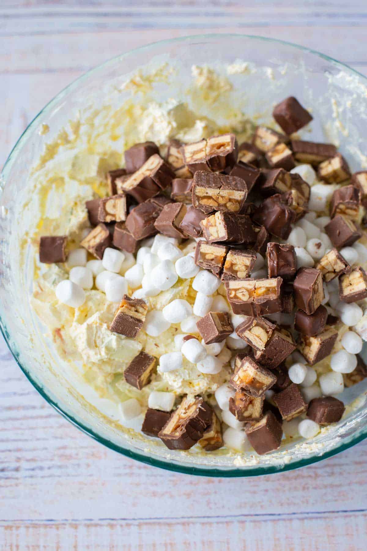 The snicker salad ingredients are ready to be stirred in the mixing bowl.