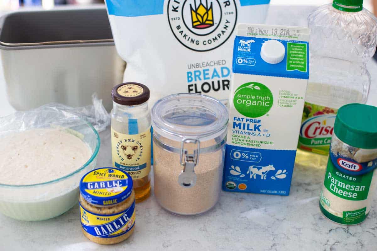 The ingredients to make homemade sourdough bread are on the counter next to the bread machine pan.