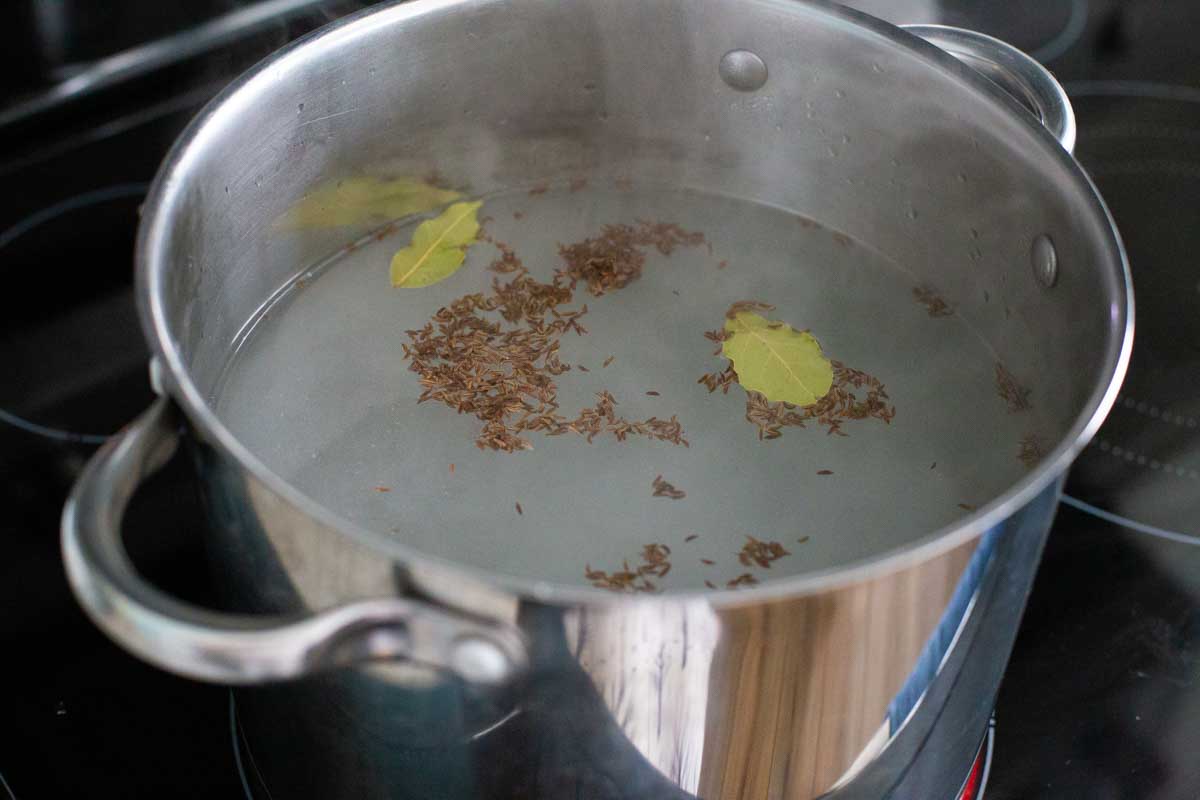 Caraway seeds and bay leaves have been added to a large pot of water for boiling.