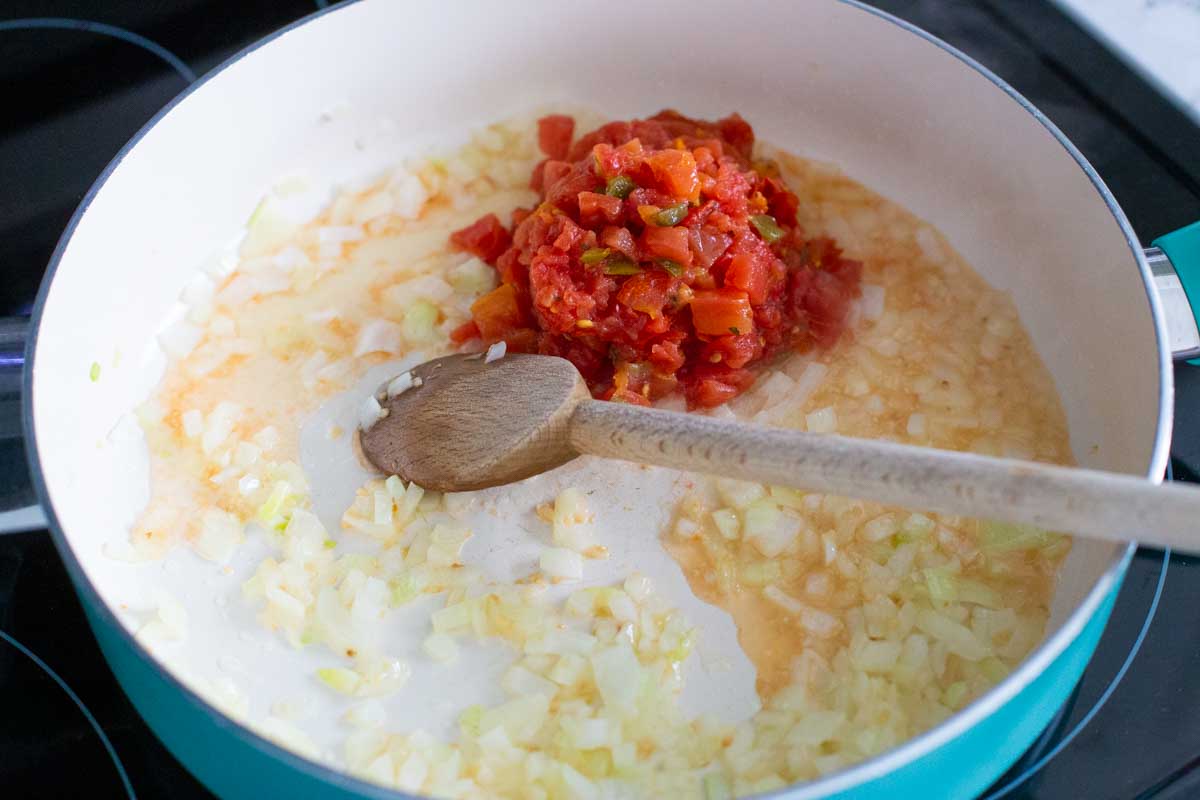 The onions and can of Rotel are in a large skillet with a spoon.