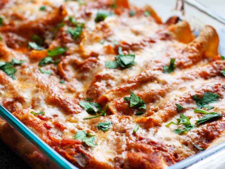 A baking pan filled with tomato sauce covered chicken enchiladas.