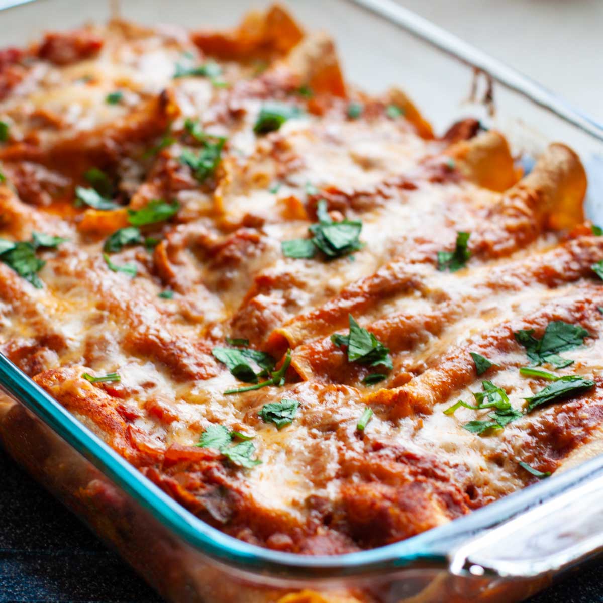 A baking pan filled with tomato sauce covered chicken enchiladas.