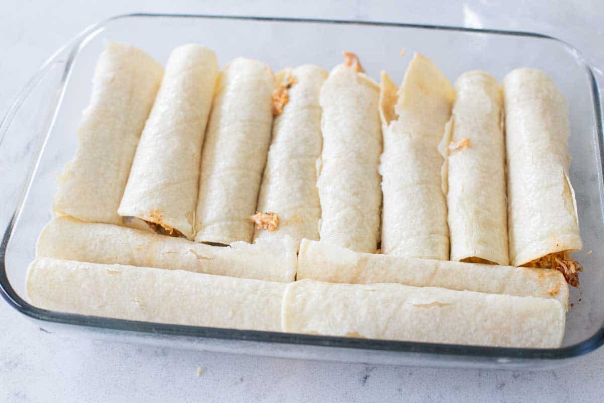 The assembled chicken enchiladas are lined up in the baking dish.