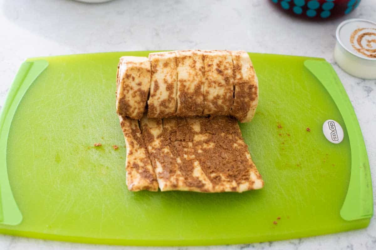 A canister of prepared cinnamon roll dough is being unrolled on a cutting board.