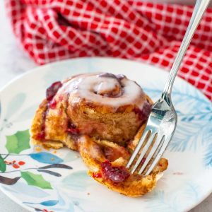 A cranberry filled cinnamon roll has a fork serving up a bite.