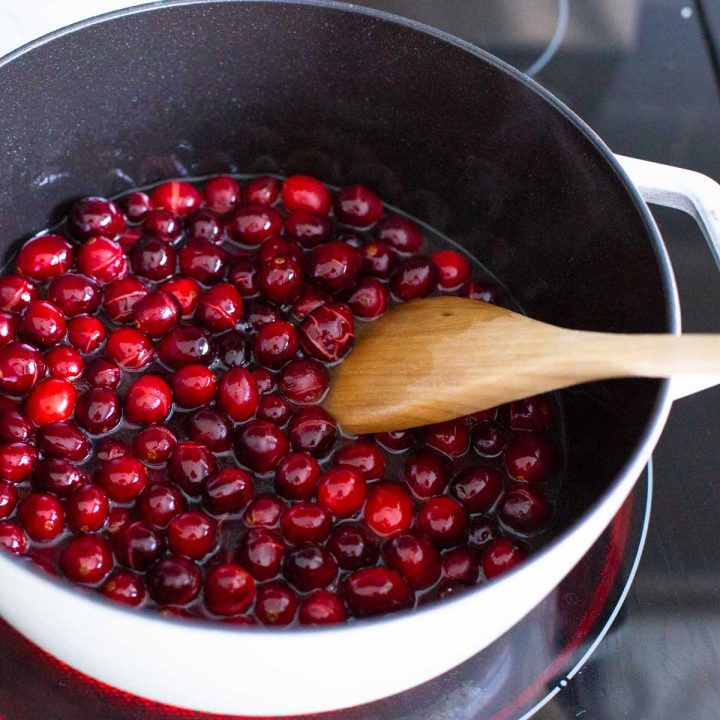 A pot of fresh cranberries is cooking with a wooden spoon to stir.