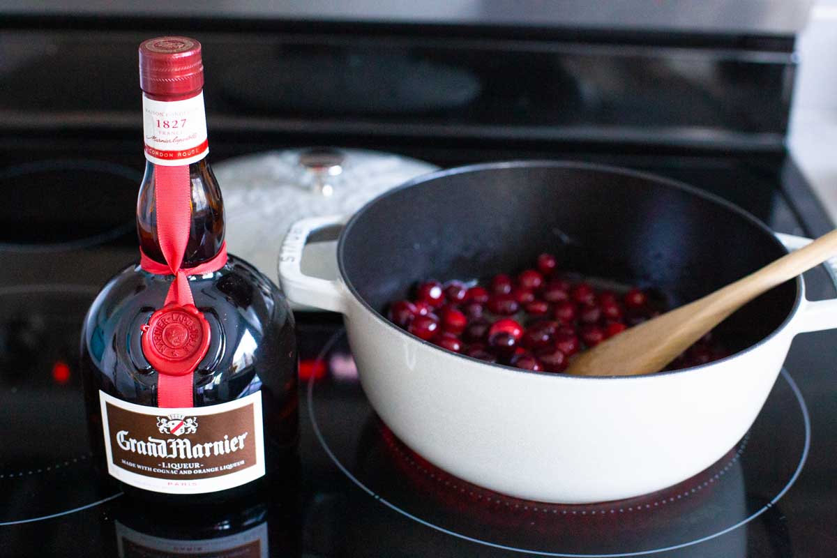 The bottle of Grand Marnier liqueur is on the stovetop next to the pot of cranberries.