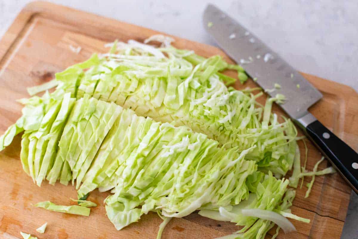 A half of a head of cabbage has been sliced on a cutting board by a large chef knife.