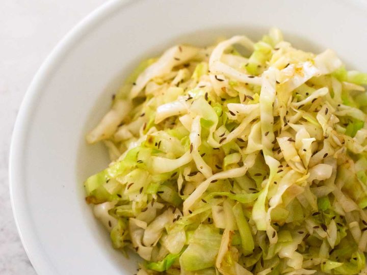 A serving of crispy fried cabbage with caraway seeds is in a white serving bowl.