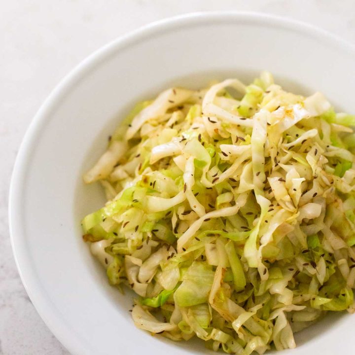 A serving of crispy fried cabbage with caraway seeds is in a white serving bowl.