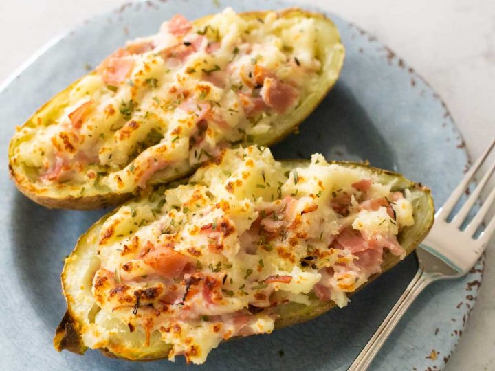 Two ham and cheese stuffed potatoes are on a serving plate with a fork.
