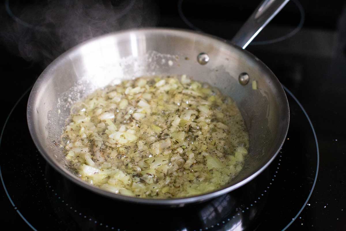 The chopped onions are being cooked in butter in a skillet and then seasoned with thyme.