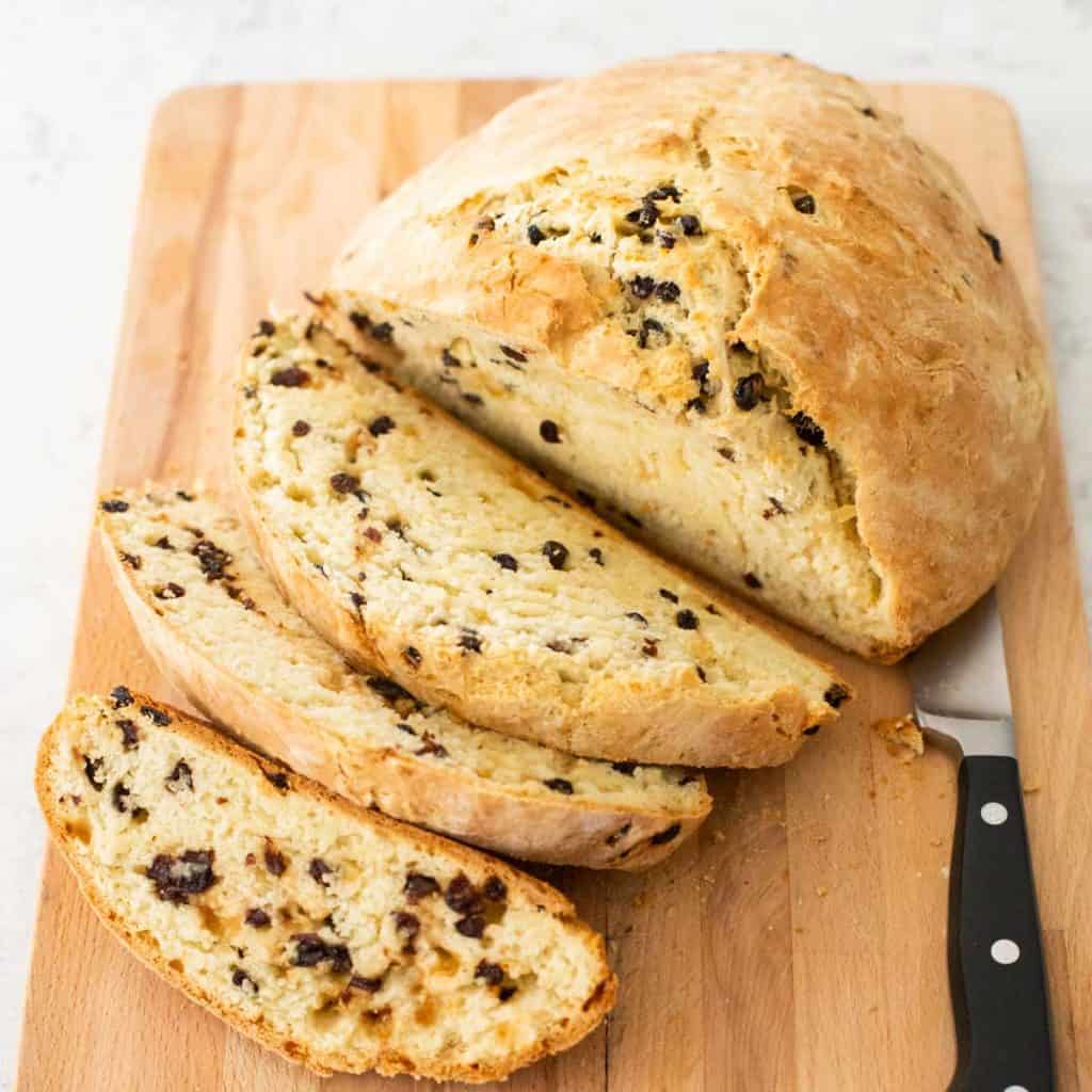 A loaf of Irish soda bread is being sliced on a bread board.