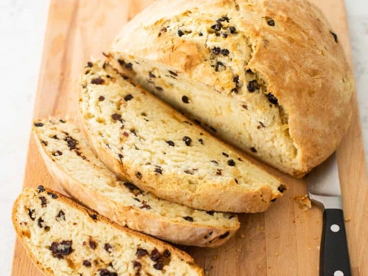 A loaf of Irish soda bread is being sliced on a bread board.