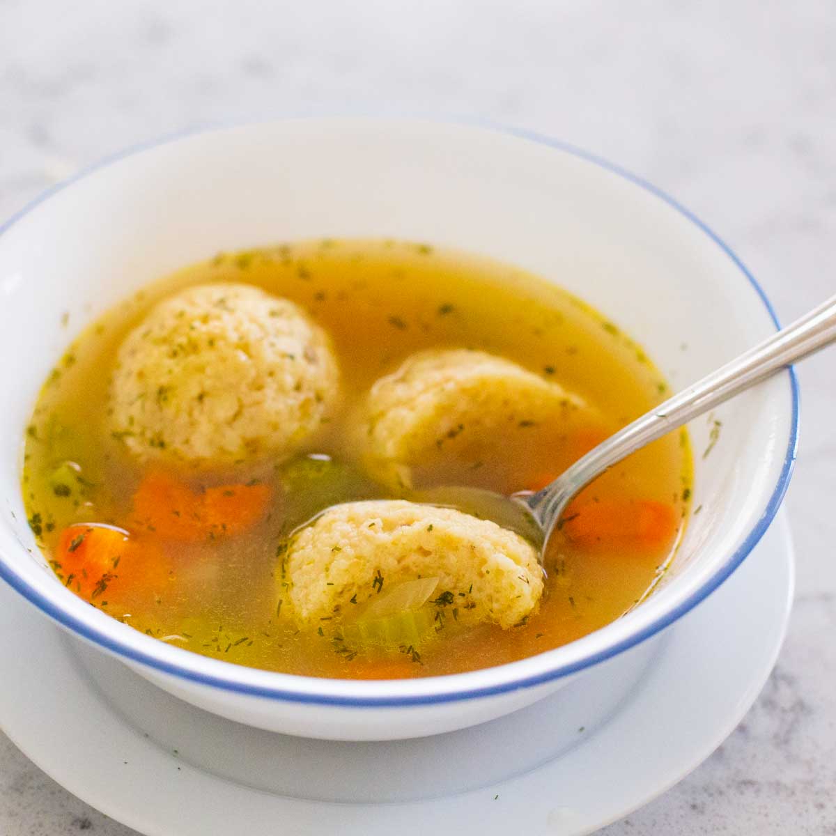 A serving of matzoh ball soup has a spoon cutting one of the balls in half to show the texture.