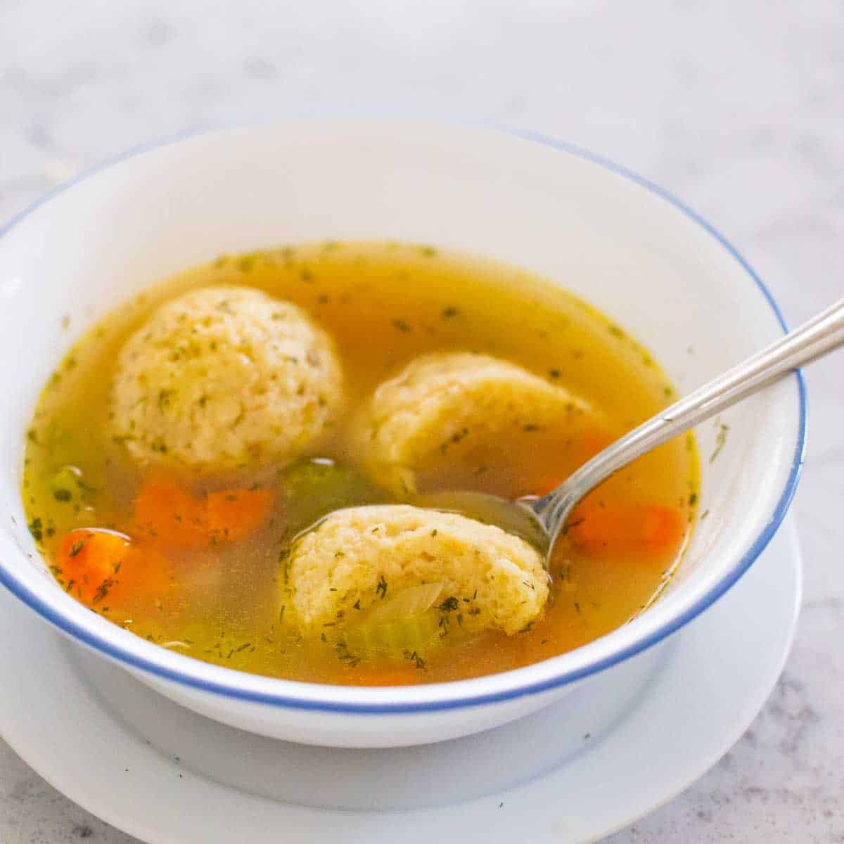 A serving of matzoh ball soup has a spoon cutting one of the balls in half to show the texture.