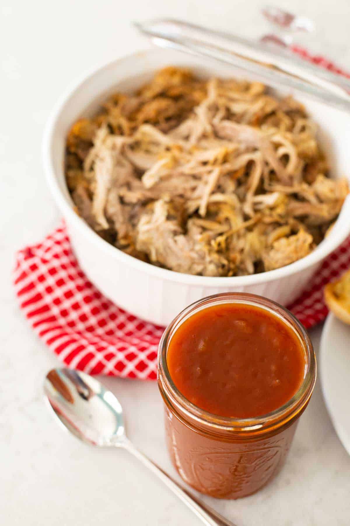 A mason jar of BBQ sauce is being served alongside pulled pork.