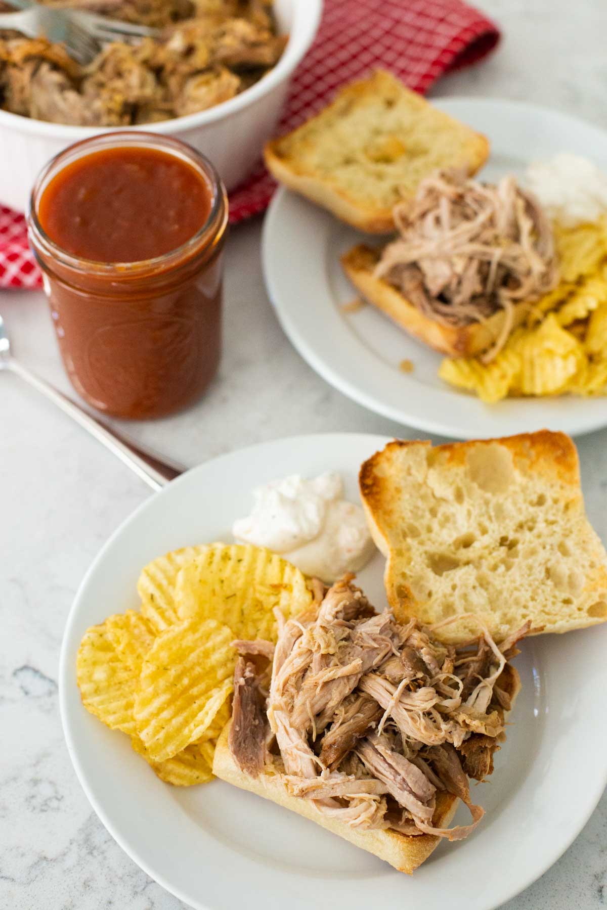 The pulled pork has been served on toasted ciabatta rolls with potato chips on the side.