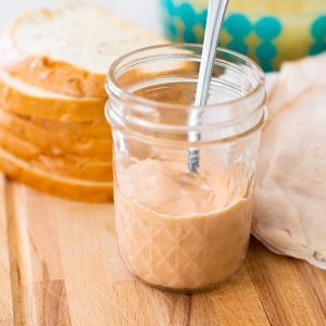 A mason jar of homemade spicy sauce in front of sliced bread.