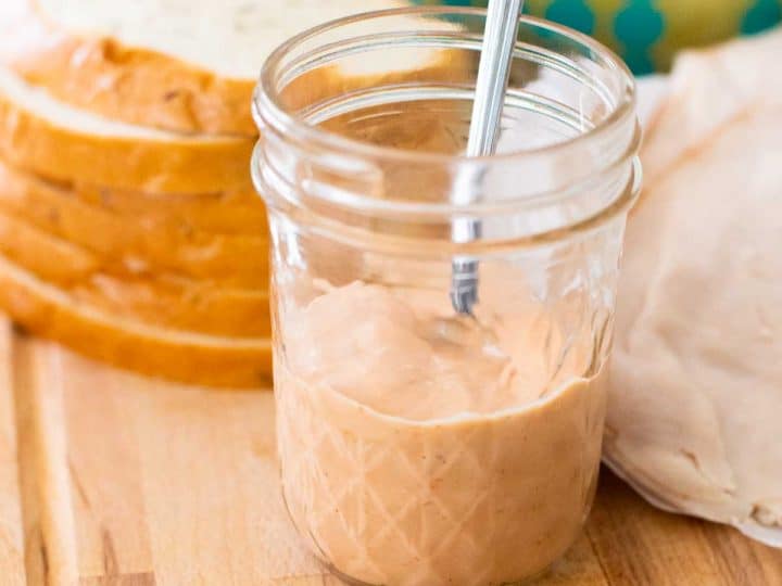 A mason jar of homemade spicy sauce in front of sliced bread.