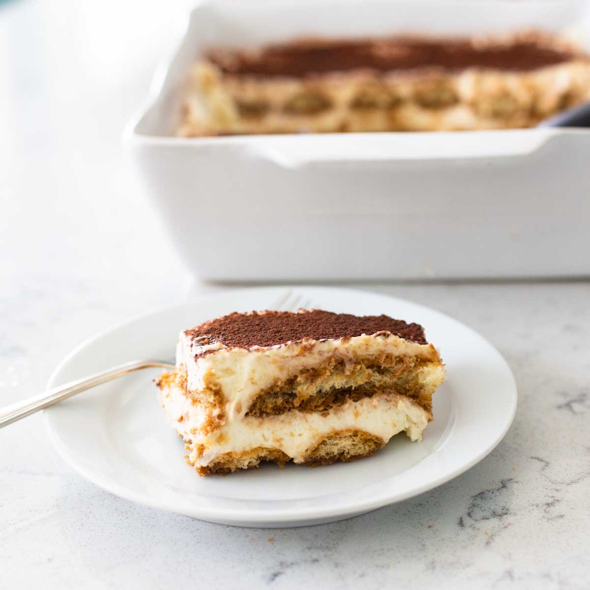 A serving of tiramisu is on a plate with a fork.