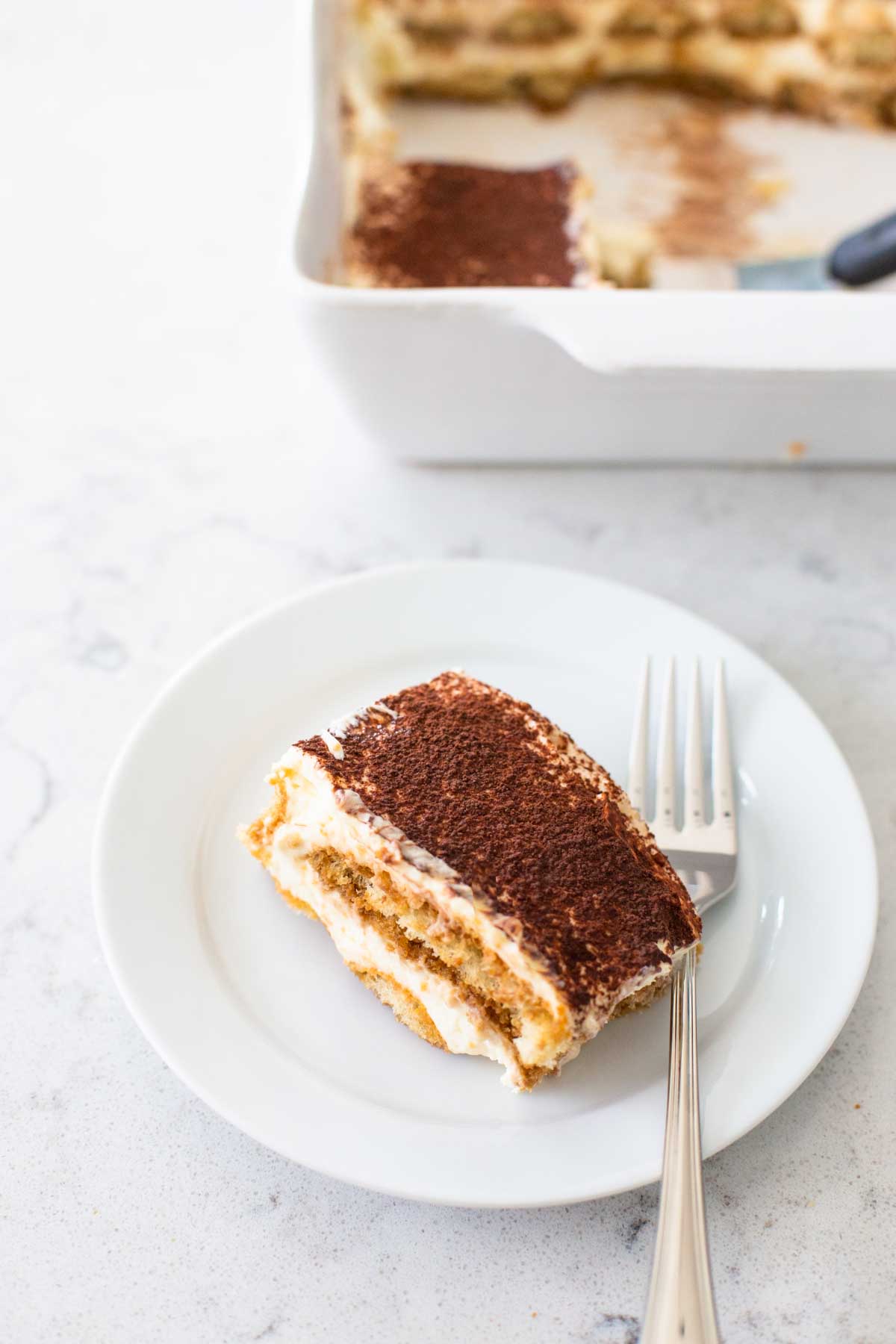 A serving of tiramisu is on a plate with a fork.